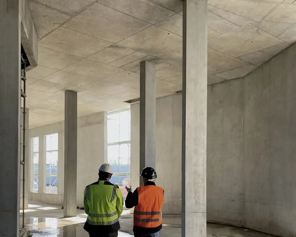 Deux responsables de chantier casqués dans la structure en béton d’un bâtiment en construction.